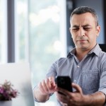 A man sitting at his desk is annoyed about a phone call he is receiving before answering it